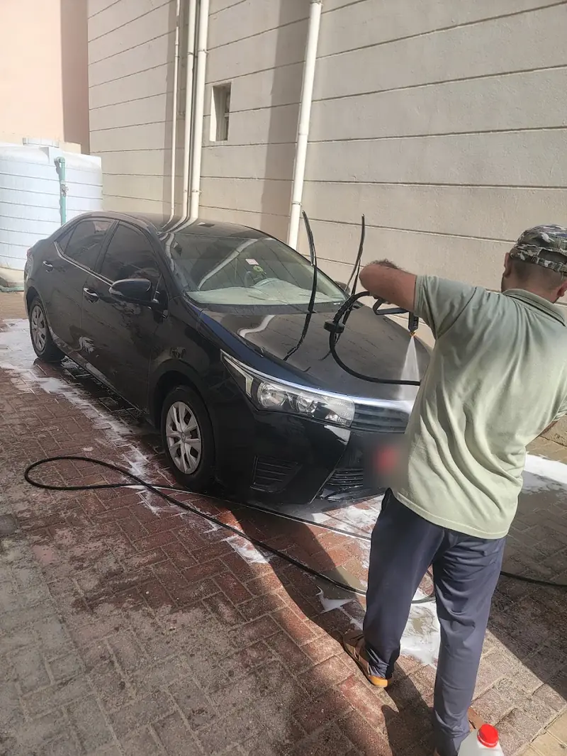 A Smart Car Cleaning washer rinsing a black car by hand